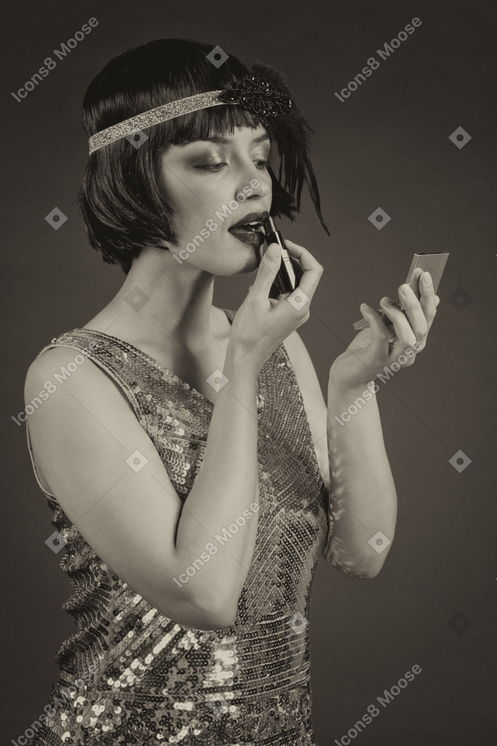 Mulher bem vestida de estilo vintage passando batom enquanto olha no espelho de mão