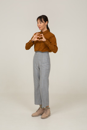 Three-quarter view of a young asian female in breeches and blouse showing heart gesture