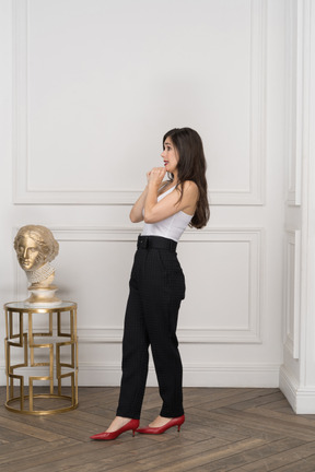 Side view of a scared female raising hands and standing near golden greek sculpture