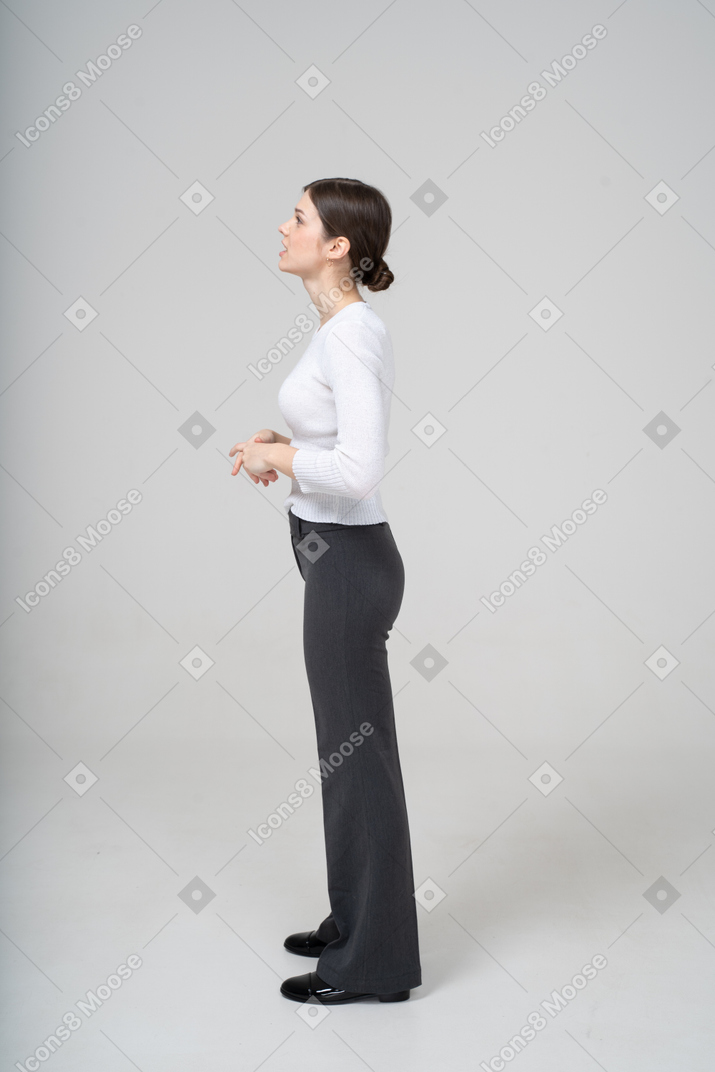 プロフィールに立っている黒いズボンと白いブラウスの若い女性