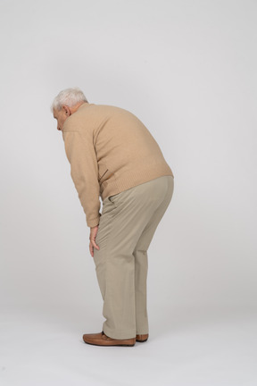 Side view of an old man in casual clothes bending down and touching his hurting knee