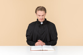 Catholic priest sitting at the table and reading a bible