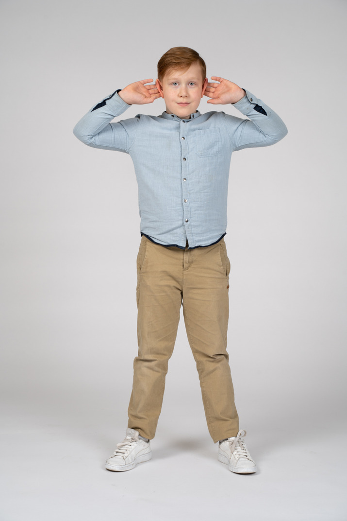 Front view of a cute boy standing with hands on head and looking at camera