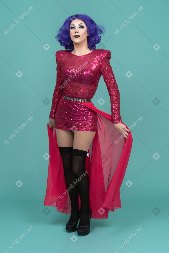 Vista frontal de una drag queen con vestido rosa alejando la falda