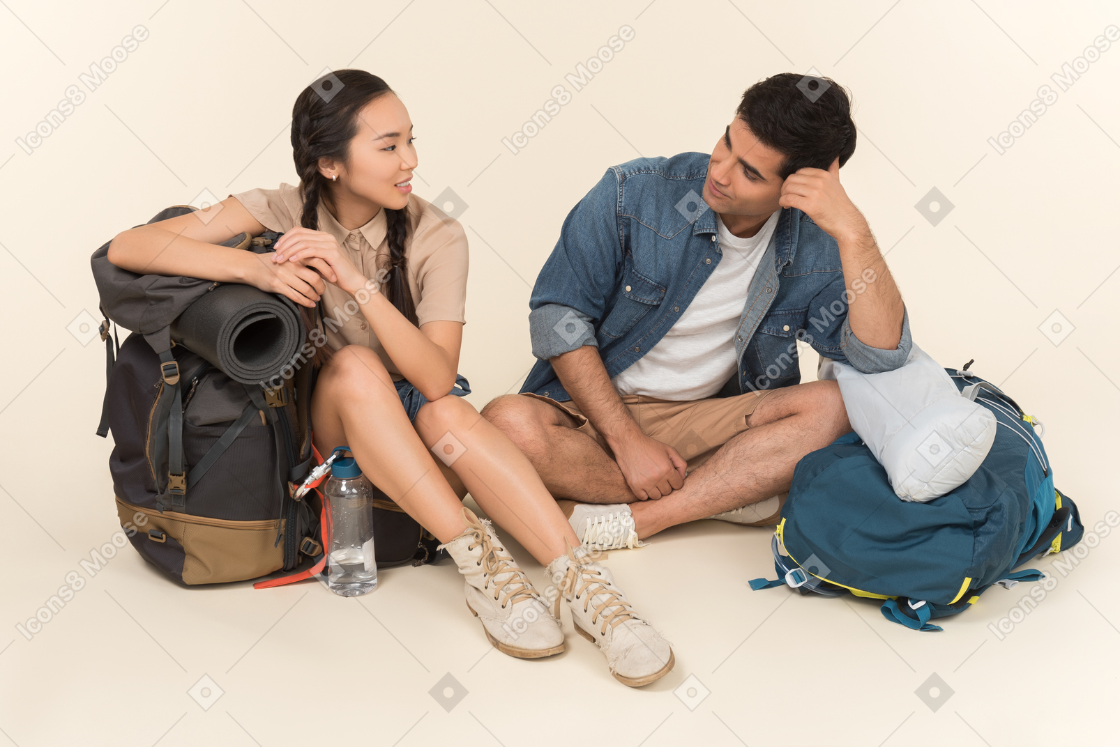Young interracial couple sitting near backpacks and talking