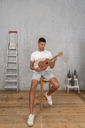 Vorderansicht eines mannes auf einem hocker, der eine ukulele untersucht