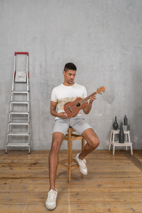 Vista frontal de um homem em um banquinho examinando um ukulele