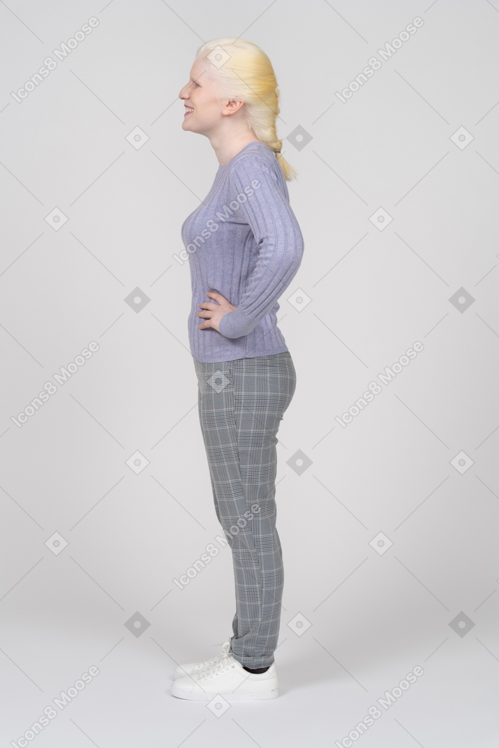 Side view of a cheerful young woman standing with hands on hips
