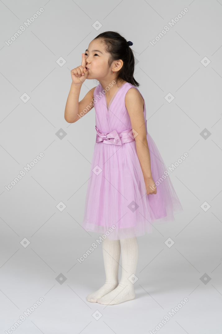 Portrait of a little girl in a pretty dress showing silence sign