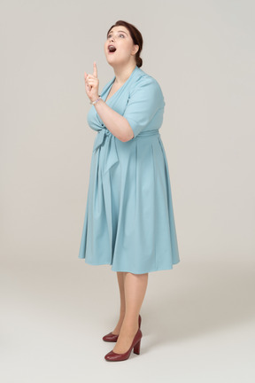 Вид сбоку на женщину в синем платье, указывая пальцем вверх