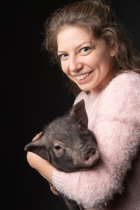 Mulher jovem feliz, segurando o porco em miniatura