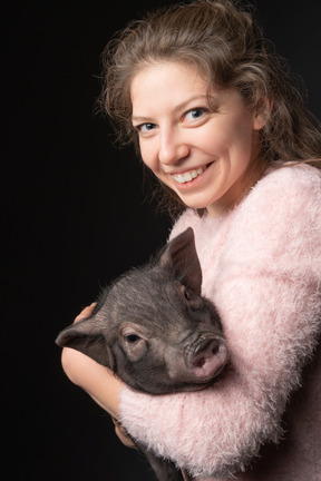 Glückliche junge frau, die miniaturschwein hält