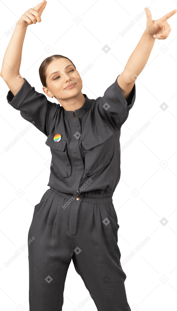 Front view of a young woman in a jumpsuit with lgbt pin raising hands