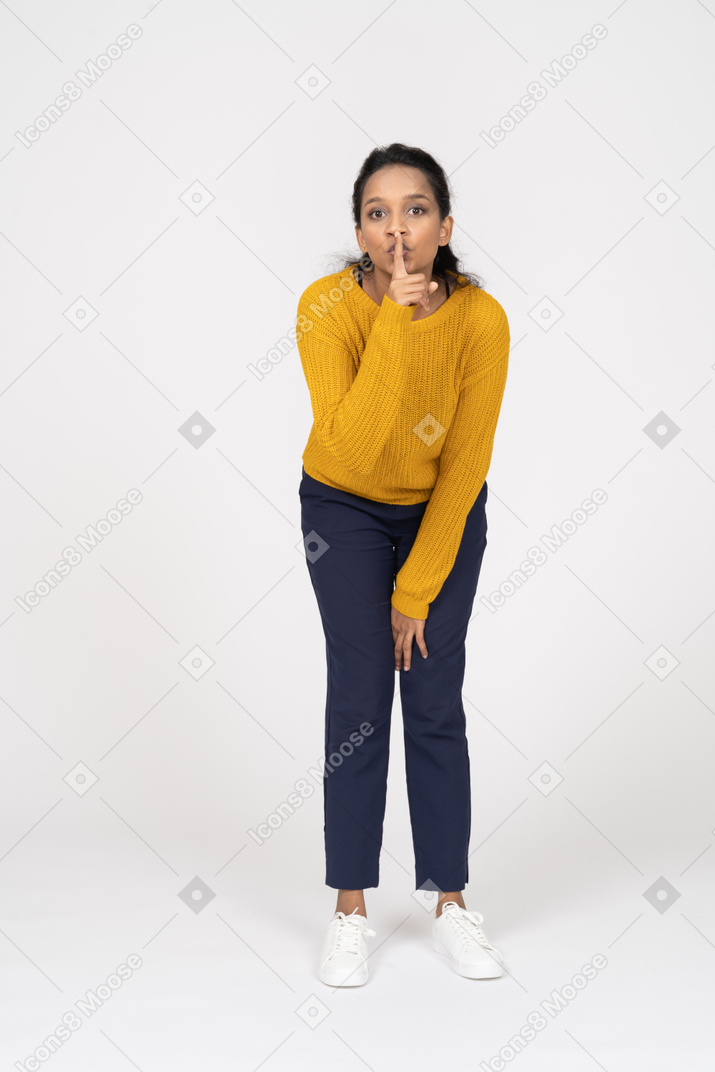 Front view of a girl in casual clothes making a shh gesture and looking at camera
