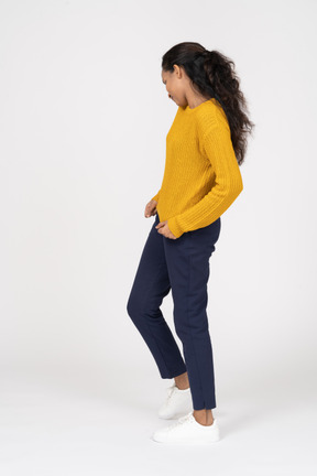 Vista lateral de uma garota com roupas casuais em pé com as mãos na cintura e olhando para o lado