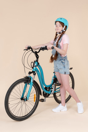 Teenage girl in blue helmet standing near blue bicycle