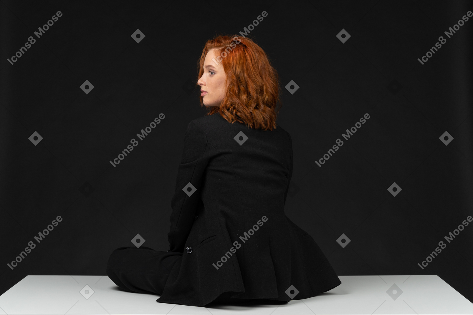 A back side view of the young woman dressed in black and sitting on the table