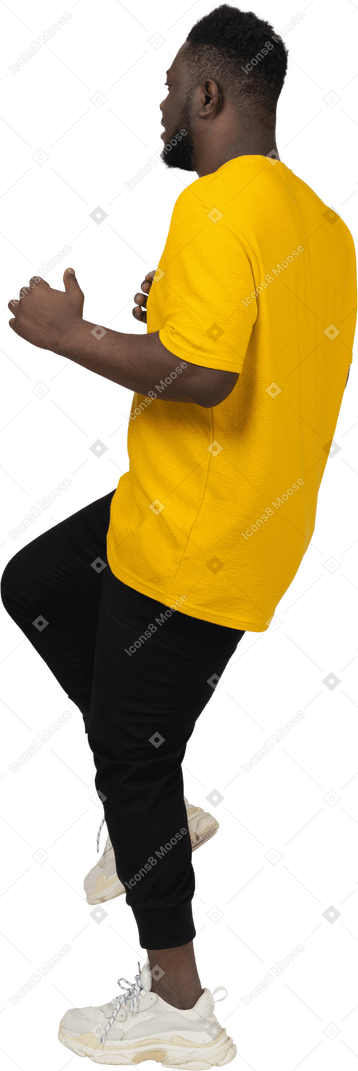 脚を上げる黄色のtシャツを着た若い浅黒い肌の男の側面図