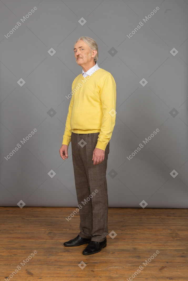 Three-quarter view of an old man in yellow pullover looking at camera