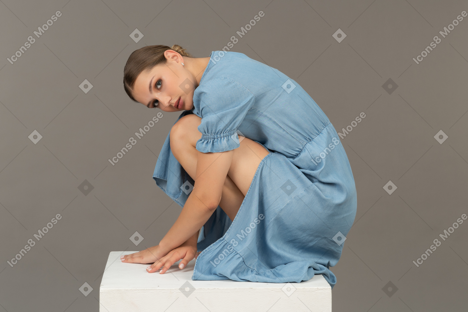 Вид сбоку на молодую женщину, сидящую на корточках на кубе