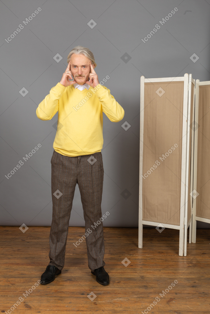 Front view of a concentrated old man touching his temples while looking at camera