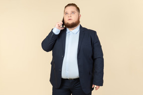 Pensativo joven trabajador de oficina con sobrepeso hablando por teléfono