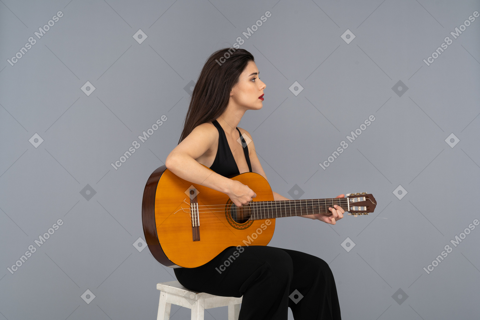 Three-quarter view of a sitting young lady in black suit holding the guitar and looking aside