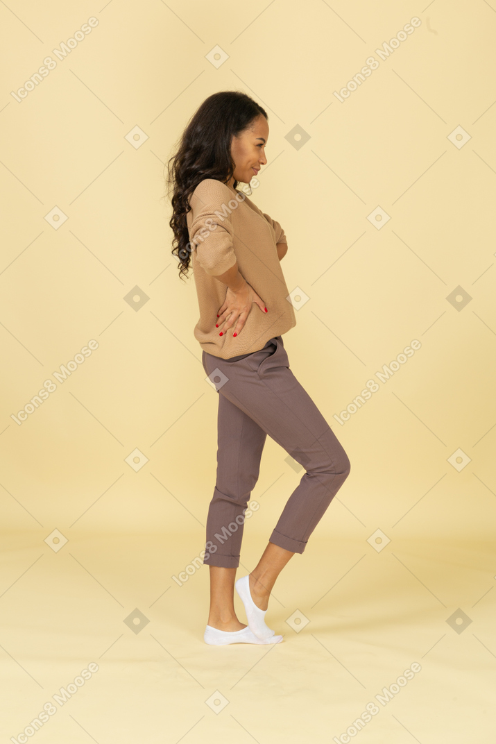 Vista lateral de una mujer joven sospechosa de piel oscura poniendo las manos en las caderas