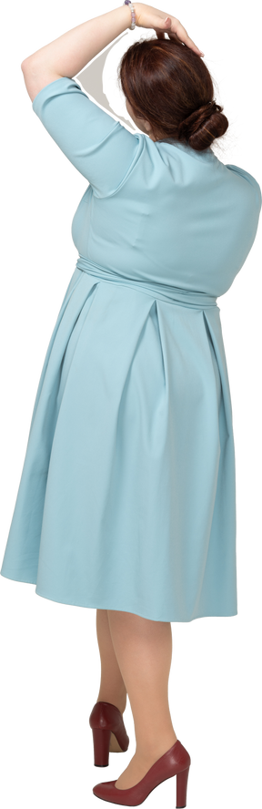Вид сзади женщины в синем платье позирует с рукой на голове