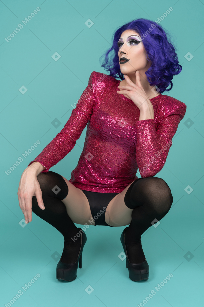 Drag queen in pink sequin dress squatting down & touching jawline