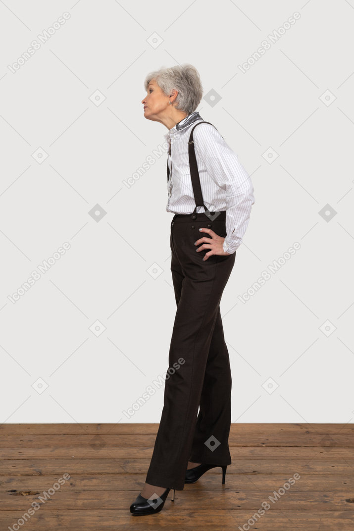 Vista lateral de uma senhora idosa descontente com roupas de escritório colocando as mãos nos quadris