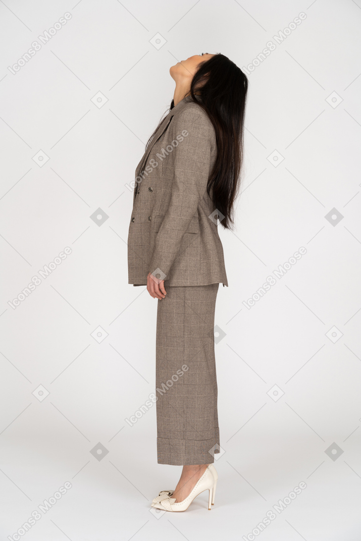 Vista lateral de una señorita en traje marrón levantando la cabeza