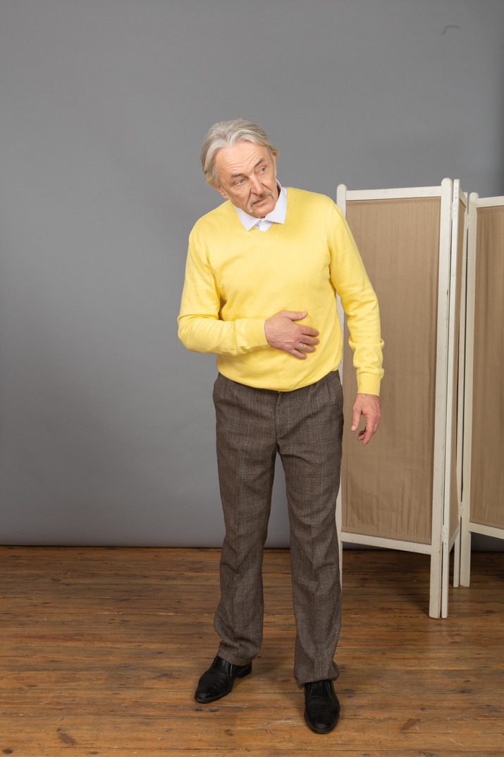 Front view of an old man putting hand on stomach while leaning forward