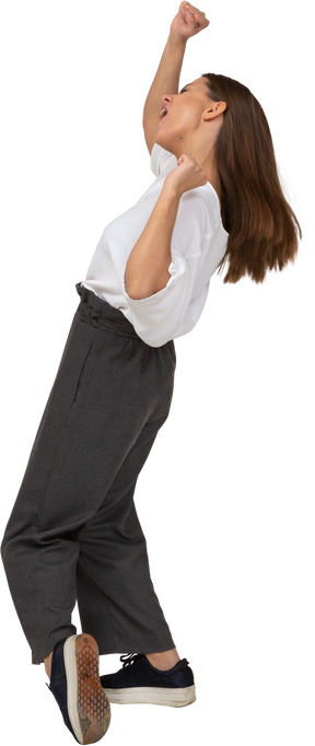 Vista lateral de una joven bailando en ropa de oficina levantando las manos