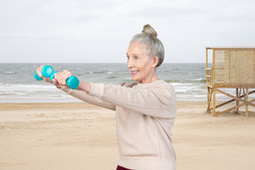 A woman holding two blue dumbs on a beach