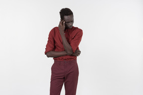 Un giovane uomo di colore in una camicia rossa con maniche arrotolate e pantaloni rosso scuro in piedi da solo sullo sfondo bianco