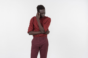 A young black man in a red shirt with rolled up sleeves and dark red pants standing alone on the white background