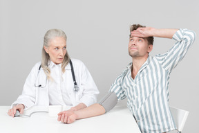 老人女性医師、若い男の血圧をチェックします。