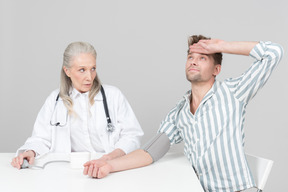 Aged female doctor checking a young man's blood pressure