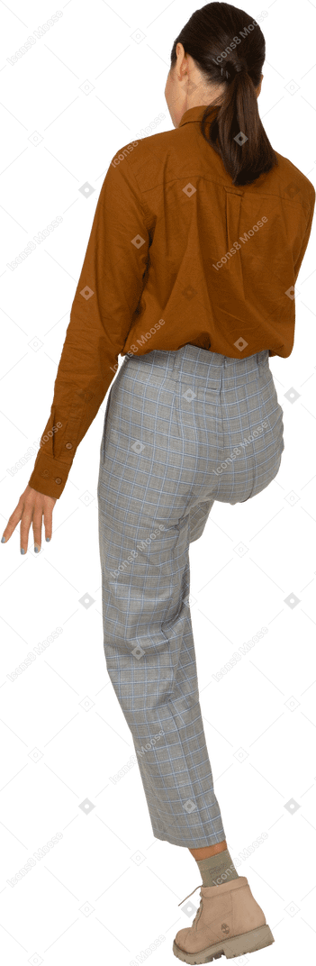 Vista posteriore di tre quarti di una giovane donna asiatica in calzoni e camicetta che alza la gamba