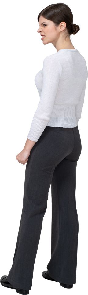 Vista posterior de tres cuartos de una mujer furiosa en ropa de oficina apretando los puños
