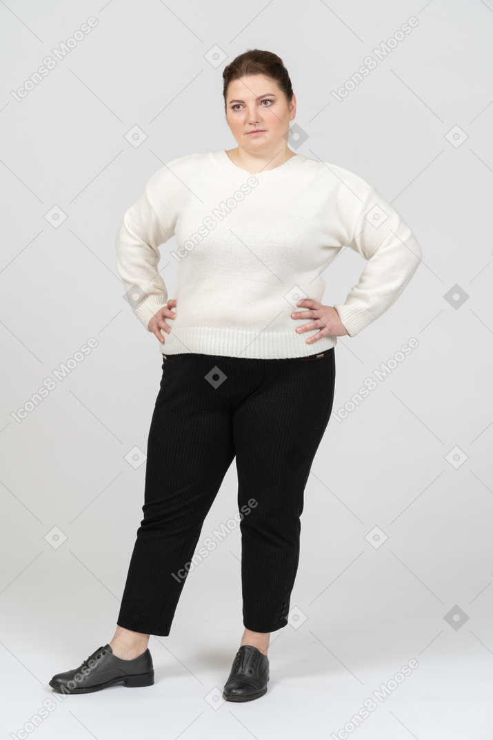 Пухлая женщина в белом свитере стоит, положив руки на бедра