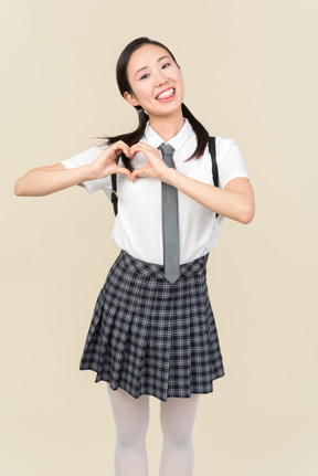 Cheerful asian school girl showing heart gesture with both hands