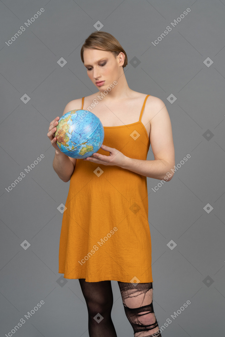 Jeune personne non binaire en robe orange tenant un globe