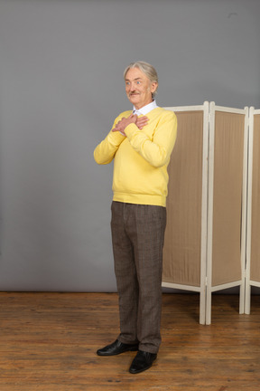 Vista de tres cuartos de un anciano sonriente cerca de la pantalla cruzando las manos