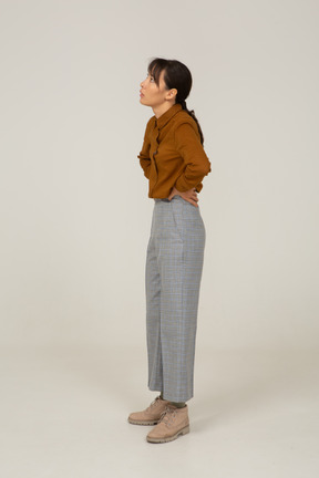 Vista di tre quarti di una giovane donna asiatica in calzoni e camicetta che mette le mani sui fianchi