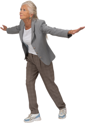 Side view of an old lady in suit balancing on one leg and outstretching arms