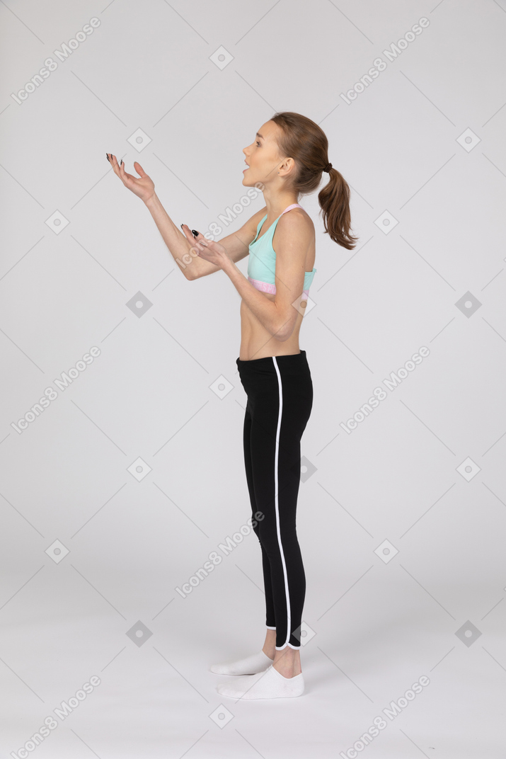 Vista lateral de una adolescente sorprendida en ropa deportiva levantando las manos