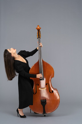 In voller länge einer jungen frau im schwarzen kleid, die kontrabass spielt, während sie sich zurücklehnt