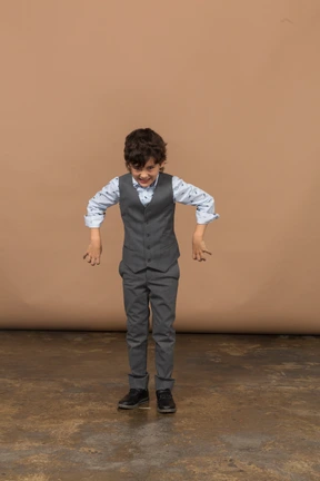 Vista frontal de un chico lindo con traje gris asustando a alguien
